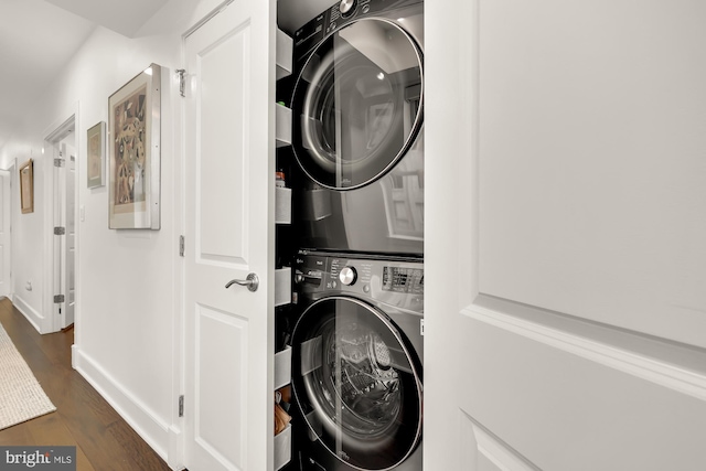 clothes washing area featuring dark wood-type flooring, laundry area, stacked washer and clothes dryer, and baseboards