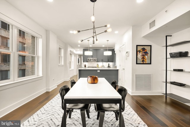 dining room with dark wood-type flooring, an inviting chandelier, visible vents, and baseboards