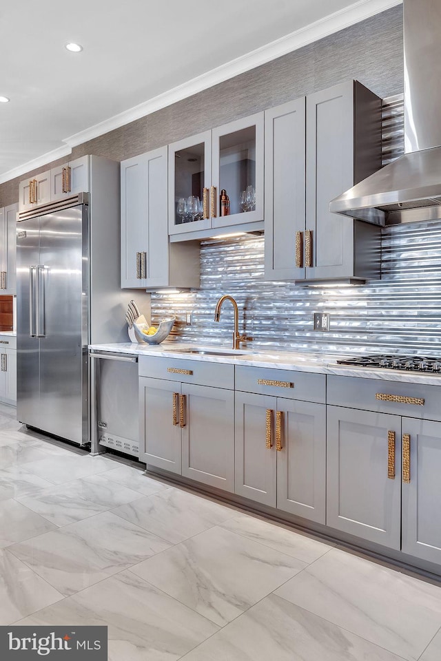 kitchen with wall chimney range hood, gray cabinetry, stainless steel built in refrigerator, gas stovetop, and ornamental molding