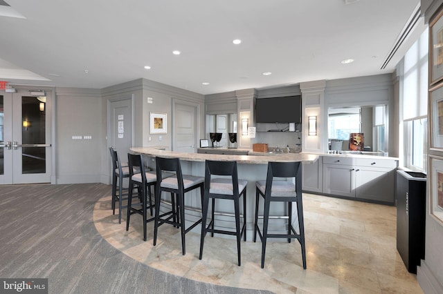 kitchen featuring gray cabinetry, a kitchen breakfast bar, light stone countertops, a kitchen island, and french doors