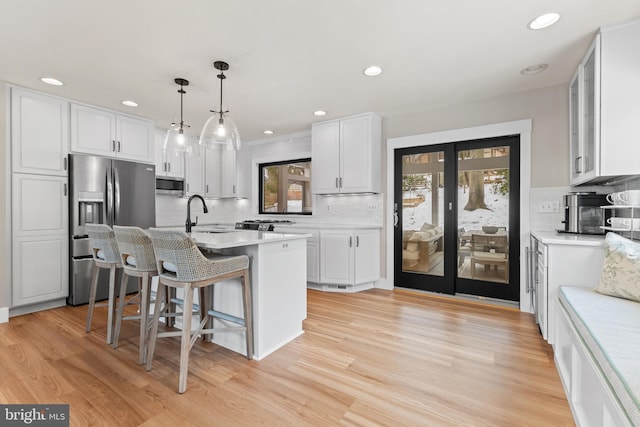 kitchen featuring a center island with sink, appliances with stainless steel finishes, hanging light fixtures, white cabinets, and a breakfast bar