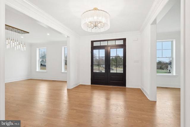 foyer entrance featuring light wood-type flooring, french doors, a notable chandelier, and crown molding