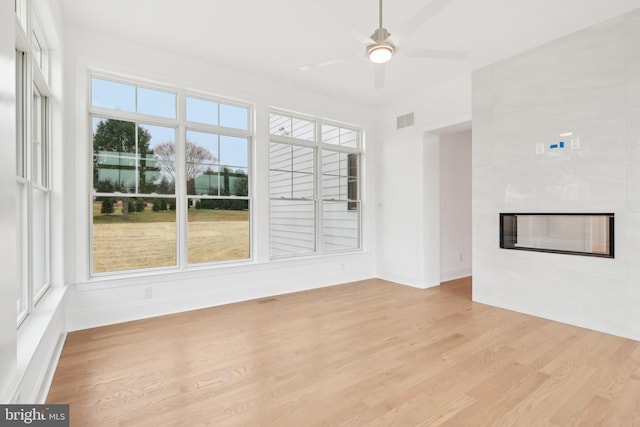 unfurnished living room featuring a large fireplace, light wood-type flooring, ceiling fan, and a healthy amount of sunlight