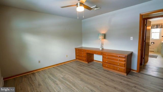 unfurnished office with built in desk, baseboard heating, ceiling fan, and light hardwood / wood-style flooring