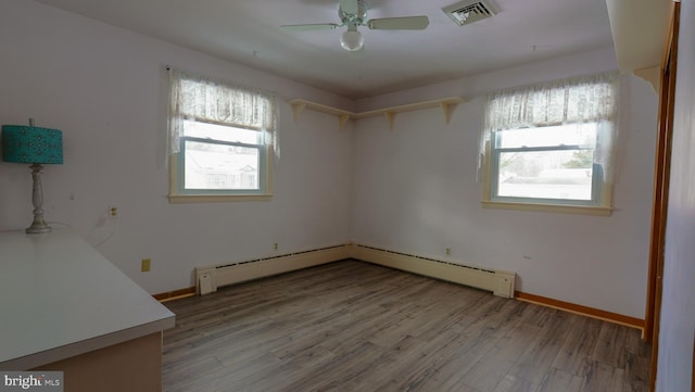 empty room featuring ceiling fan, a baseboard radiator, hardwood / wood-style floors, and a healthy amount of sunlight