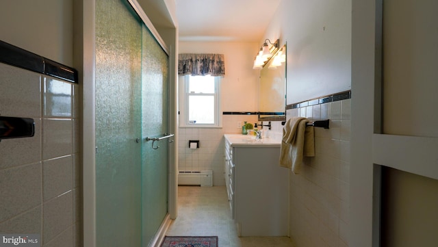 bathroom featuring a baseboard heating unit, a shower with door, vanity, and tile walls