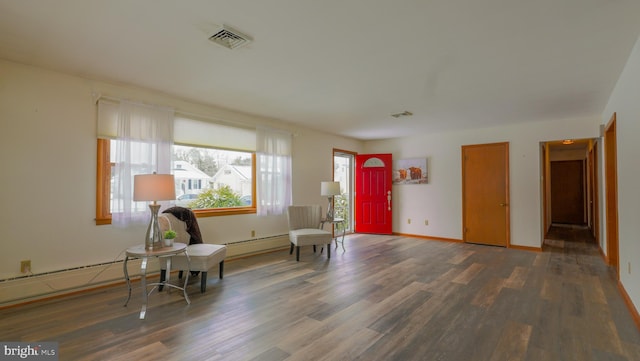 sitting room featuring dark wood-type flooring, a baseboard heating unit, and a healthy amount of sunlight