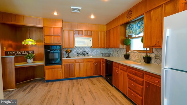 kitchen featuring sink, tasteful backsplash, light hardwood / wood-style flooring, hanging light fixtures, and black appliances