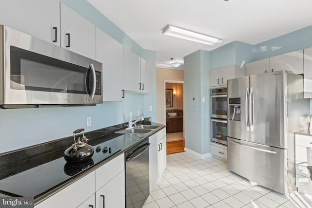 kitchen with stainless steel appliances, light tile patterned flooring, sink, and white cabinets