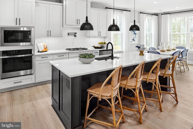 kitchen featuring stainless steel appliances, sink, white cabinetry, light wood-type flooring, and a kitchen island with sink