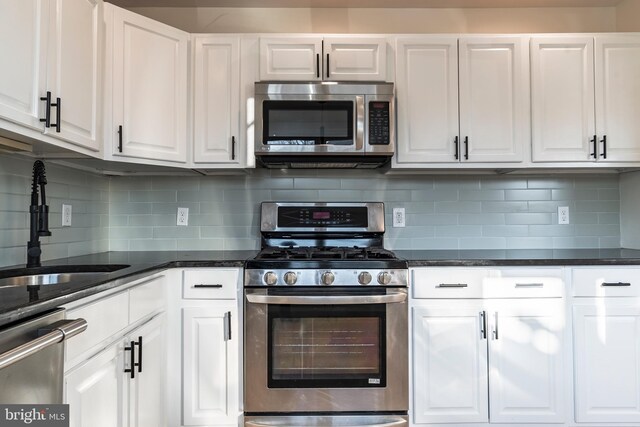 kitchen with stainless steel appliances, backsplash, white cabinets, dark stone countertops, and sink