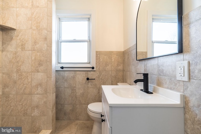 bathroom featuring toilet, vanity, tile walls, and plenty of natural light