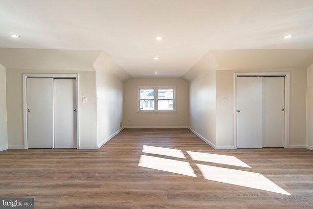 unfurnished bedroom with lofted ceiling, multiple closets, and light wood-type flooring