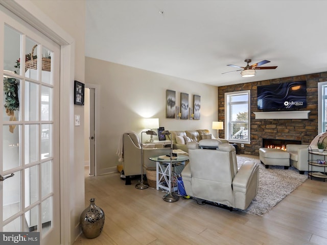 living room with light wood-type flooring, ceiling fan, and a fireplace