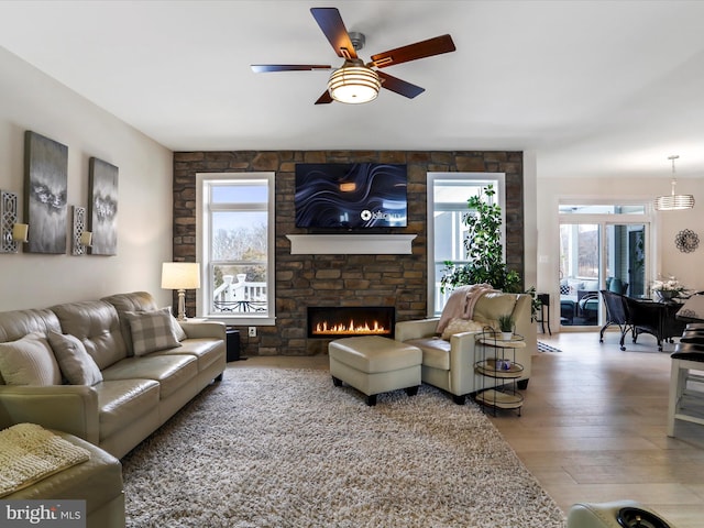 living room with ceiling fan, light hardwood / wood-style flooring, and a stone fireplace