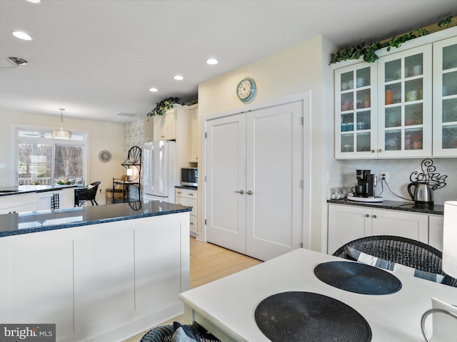 kitchen with white fridge, decorative backsplash, decorative light fixtures, white cabinets, and light hardwood / wood-style flooring