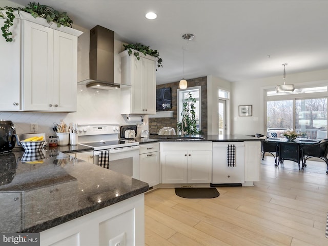 kitchen featuring wall chimney range hood, hanging light fixtures, white electric range oven, white cabinets, and dishwashing machine