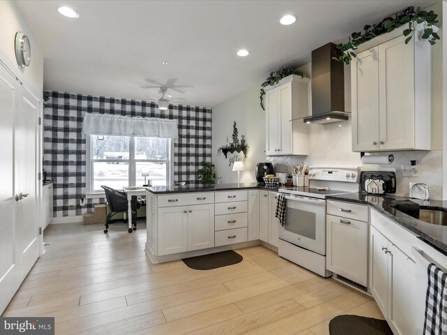 kitchen with kitchen peninsula, white appliances, white cabinets, and wall chimney exhaust hood