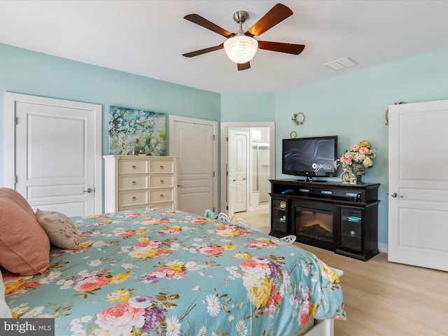 bedroom with light wood-type flooring, ceiling fan, and ensuite bath