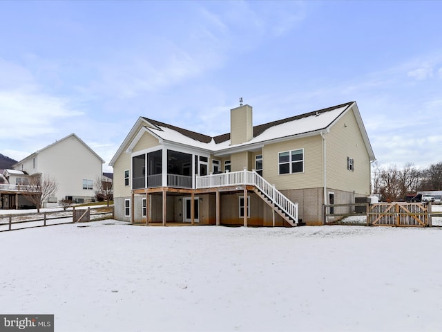 snow covered property with a wooden deck and a sunroom