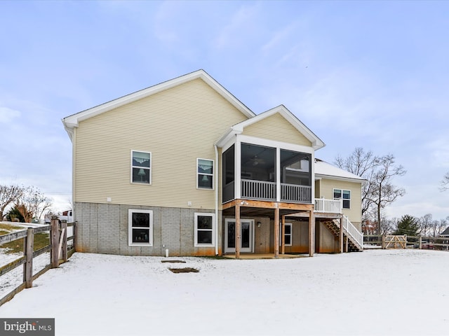 snow covered back of property featuring a wooden deck and a sunroom