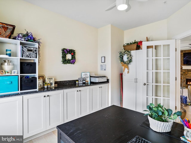 interior space with ceiling fan, dark stone countertops, a stone fireplace, and white cabinetry