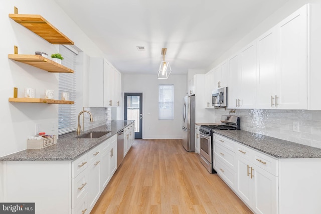 kitchen featuring white cabinets, stainless steel appliances, dark stone counters, tasteful backsplash, and sink