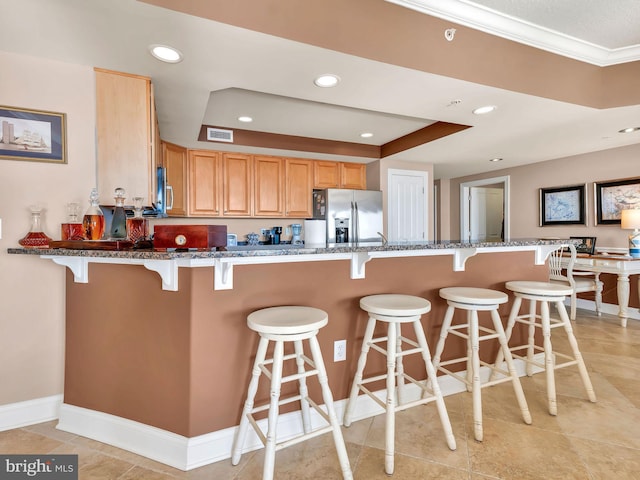 kitchen with kitchen peninsula, stainless steel refrigerator with ice dispenser, a raised ceiling, crown molding, and a breakfast bar