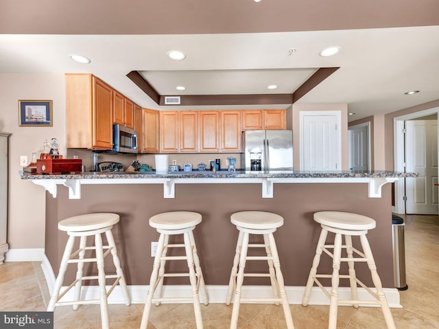 kitchen with a breakfast bar area, appliances with stainless steel finishes, a tray ceiling, and dark stone counters