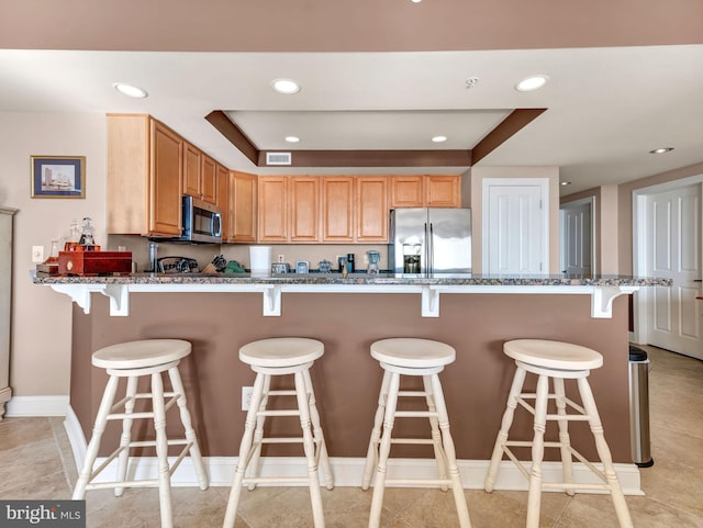 kitchen with stainless steel appliances, a kitchen bar, and stone countertops