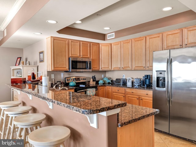 kitchen featuring kitchen peninsula, appliances with stainless steel finishes, dark stone countertops, and a kitchen bar