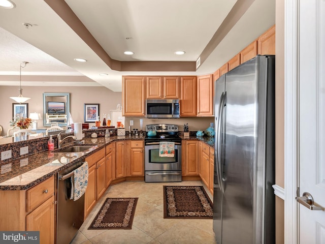 kitchen featuring kitchen peninsula, stainless steel appliances, decorative light fixtures, dark stone counters, and sink