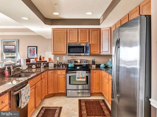 kitchen with kitchen peninsula, appliances with stainless steel finishes, a raised ceiling, dark stone counters, and sink