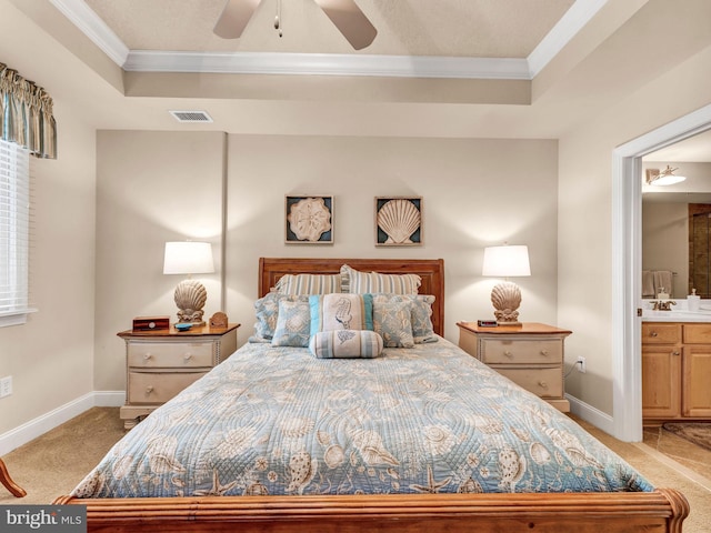 carpeted bedroom with ceiling fan, crown molding, ensuite bathroom, and a raised ceiling