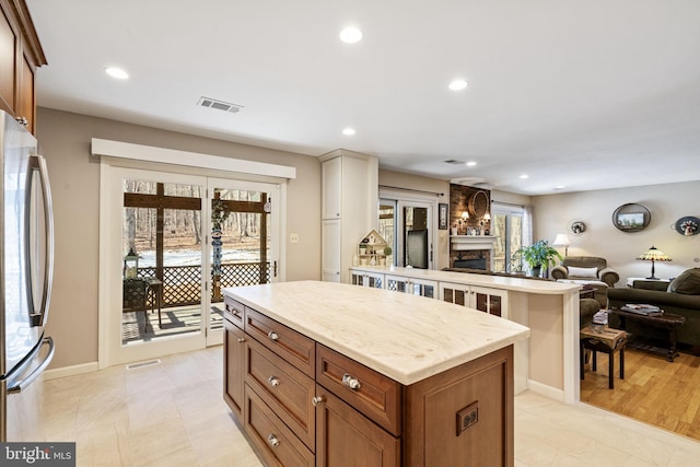 kitchen with a stone fireplace, a wealth of natural light, stainless steel refrigerator, and a kitchen island