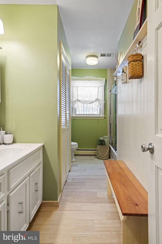 bathroom featuring hardwood / wood-style flooring, vanity, a baseboard heating unit, toilet, and a shower with door