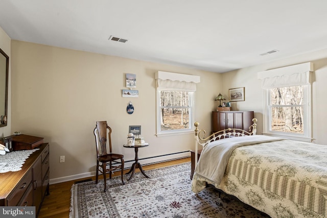 bedroom with multiple windows, a baseboard heating unit, and hardwood / wood-style flooring