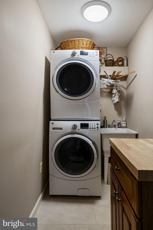 laundry area featuring stacked washer / dryer, light tile patterned floors, and cabinets