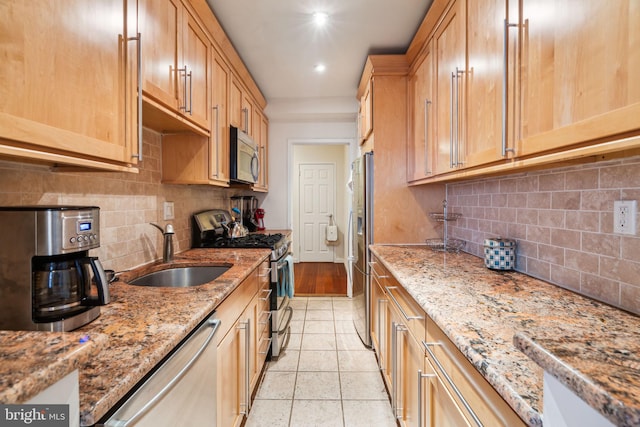 kitchen with tasteful backsplash, appliances with stainless steel finishes, sink, and light stone counters