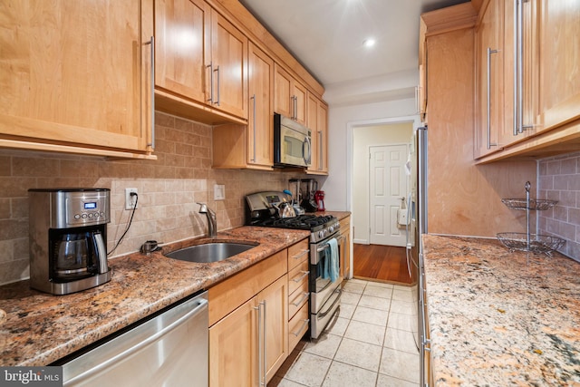 kitchen with sink, light tile patterned floors, appliances with stainless steel finishes, light stone countertops, and decorative backsplash