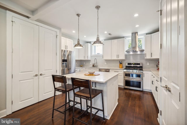 kitchen featuring a kitchen island, stainless steel appliances, wall chimney exhaust hood, and white cabinetry