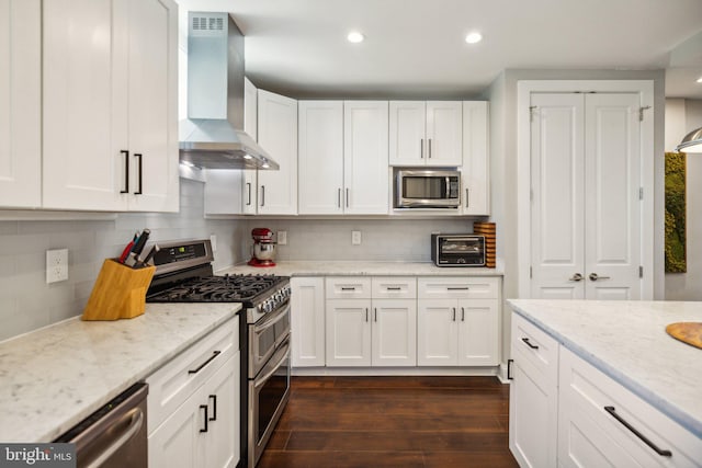 kitchen with white cabinetry, wall chimney exhaust hood, light stone countertops, dark hardwood / wood-style flooring, and appliances with stainless steel finishes