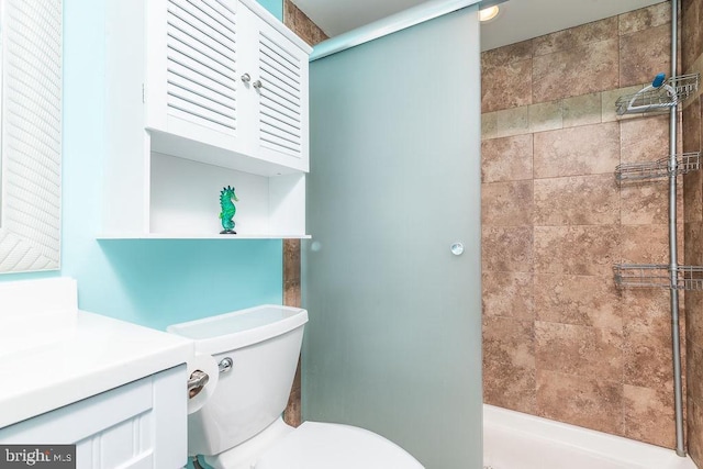 bathroom featuring toilet, tiled shower, and vanity