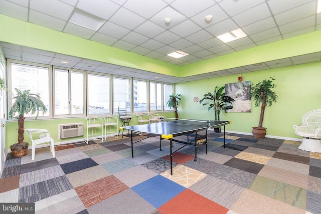 game room featuring an AC wall unit, a wealth of natural light, a drop ceiling, and dark carpet