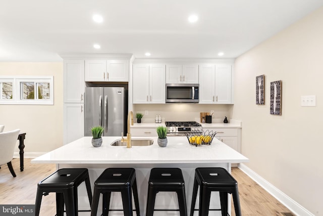 kitchen with appliances with stainless steel finishes, a breakfast bar, white cabinetry, and sink