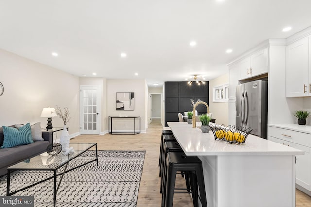 kitchen with white cabinetry, light hardwood / wood-style flooring, an island with sink, a breakfast bar area, and stainless steel fridge