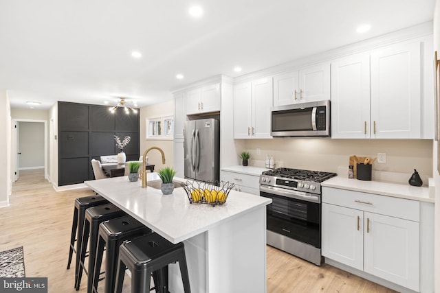 kitchen featuring a center island with sink, light hardwood / wood-style floors, white cabinetry, appliances with stainless steel finishes, and a kitchen breakfast bar