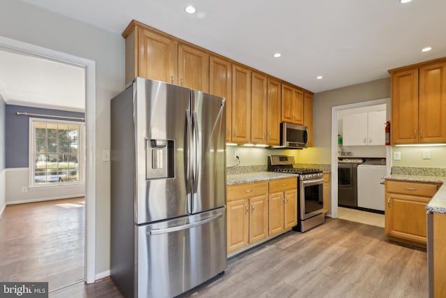 kitchen with light stone countertops, appliances with stainless steel finishes, independent washer and dryer, and light hardwood / wood-style floors