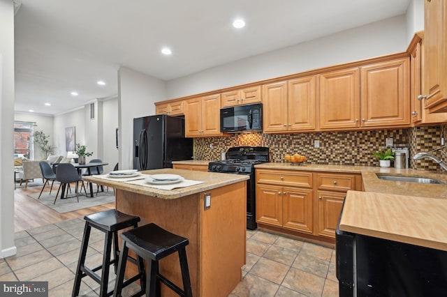 kitchen with black appliances, a kitchen island, sink, backsplash, and a breakfast bar