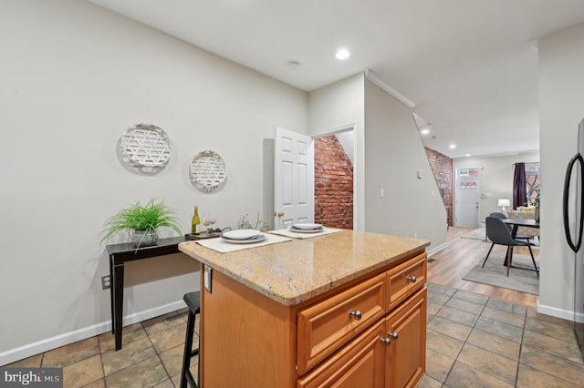 kitchen featuring a kitchen island, a kitchen bar, fridge, and light stone countertops